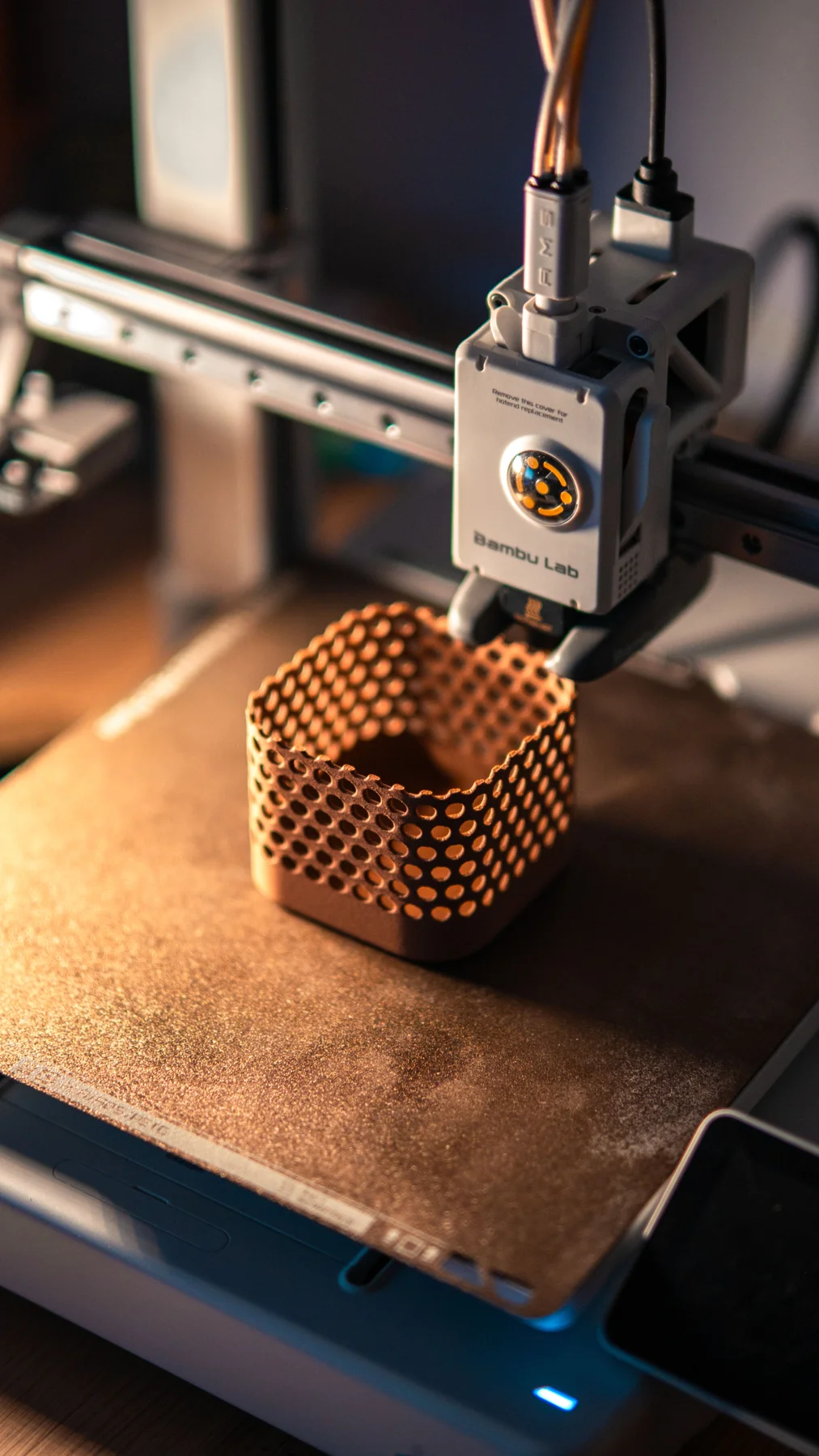 Impresora 3D junto a una pieza cilíndrica perforada. Fotografía de stock referencial.